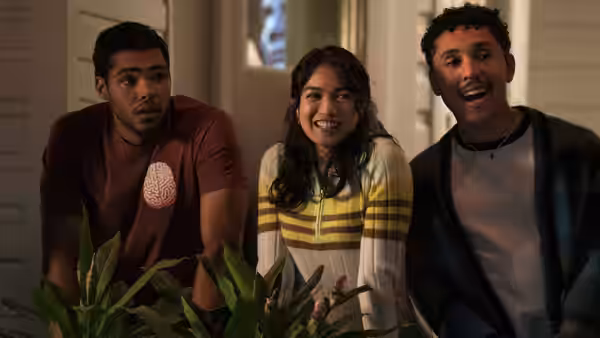Three young adults sit together indoors, smiling and looking toward someone offscreen