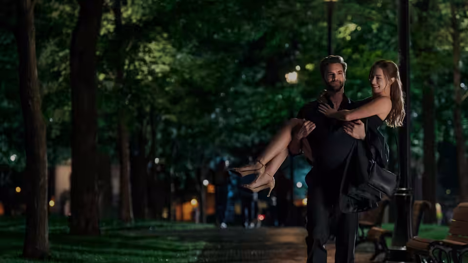 Dr. Adam Carlsen (Tom Bateman) carries Olive Smith (Lili Reinhart) through a tree-lined park
