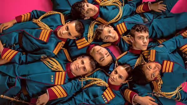 Students in teal uniforms lie clustered together on a bright pink floor