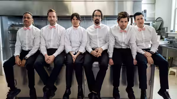 Catering crew in pink bow ties sits on a stainless counter