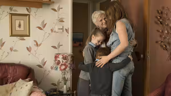 Rose-Lynn (Jessie Buckley) embraces her children and Marion (Julie Walters) in a living room