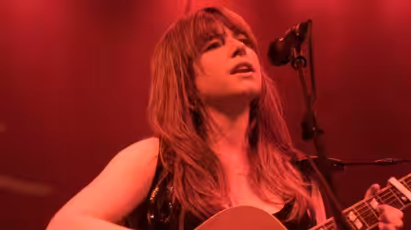 Rose-Lynn (Jessie Buckley) sings while playing acoustic guitar under red stage lights
