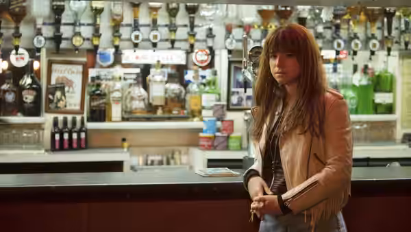Rose-Lynn (Jessie Buckley) stands at a pub bar, holding her hands together