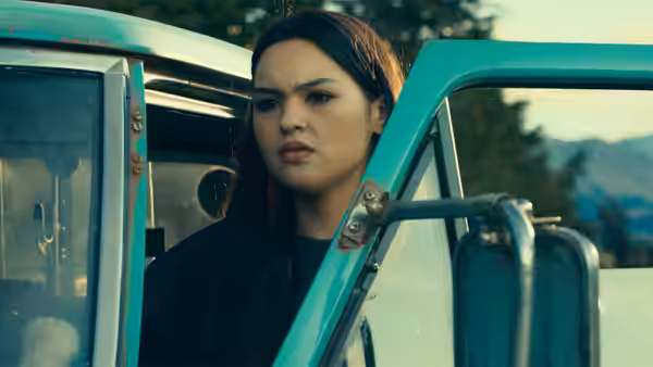 A young woman stands beside the open door of a turquoise vehicle