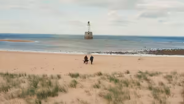 Two people walking across a sandy beach towards the sea