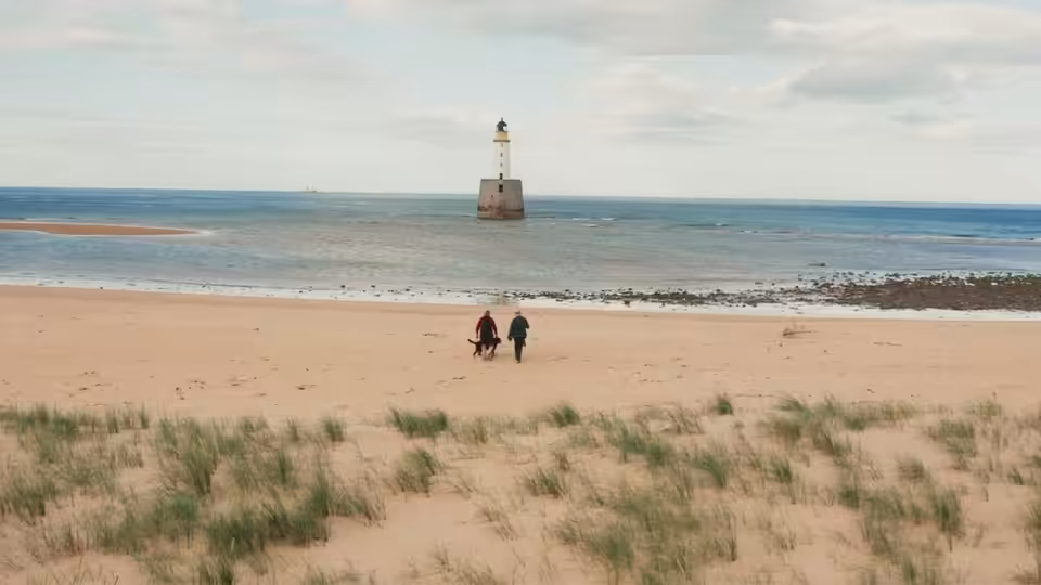 Two people walking across a sandy beach towards the sea