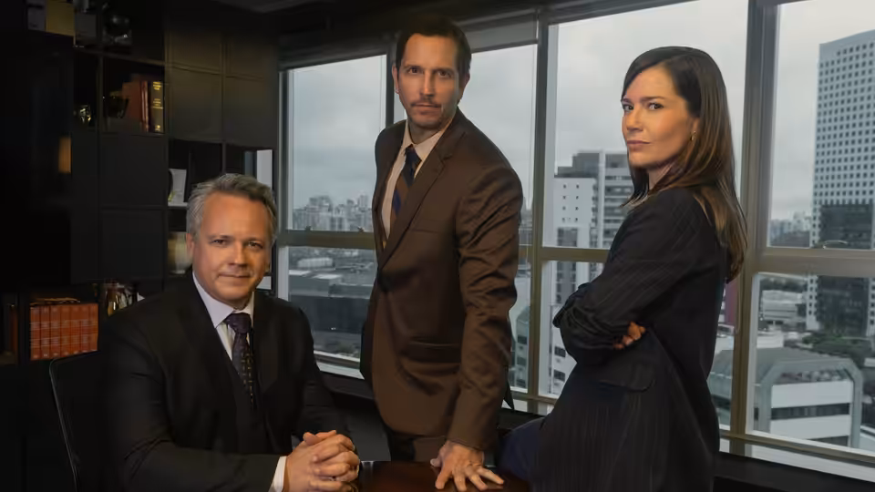 three business colleagues posing together inside a high-rise office with city views