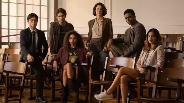 six professionals in business attire seated in rows of wooden classroom chairs