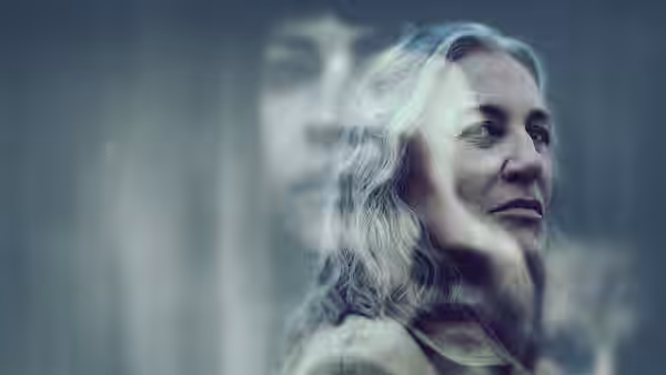 A silver-haired woman looks aside as a blurred figure looms behind her