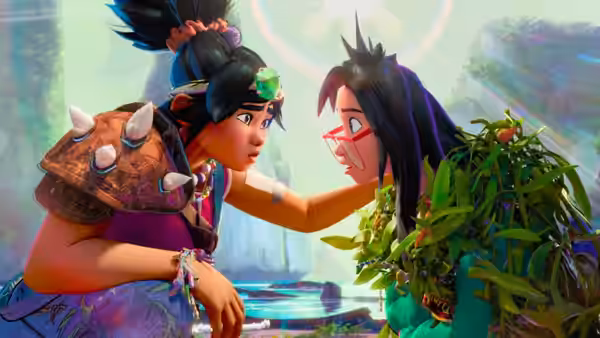 A girl in a colorful outfit touches the cheek of another girl with glasses in a jungle