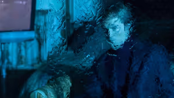 A man stands behind rippled glass in blue light