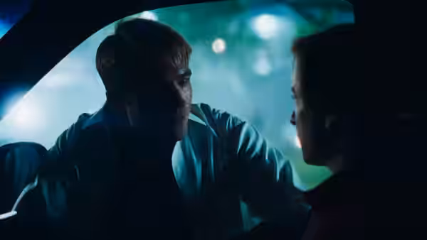 A man leans into a car to speak with a woman