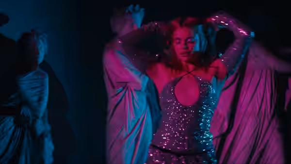 Woman in a sequined dress posing with arms raised in blue light