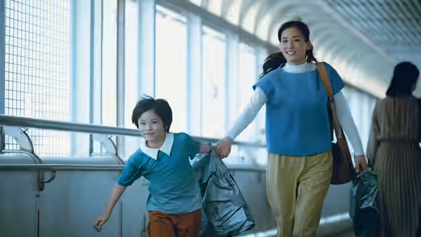 Woman and boy walk through a bright corridor holding hands with bags