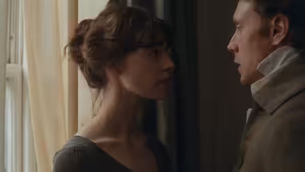 A young woman faces a gentleman closely beside a curtained window