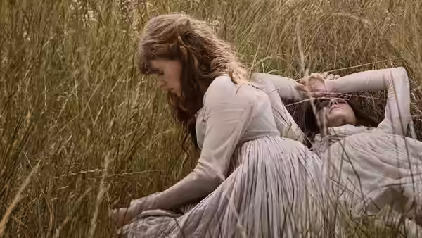 A woman leans over another reclining in tall grass