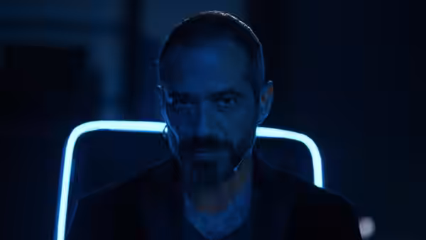 Bearded man with earpiece stares ahead under blue neon light