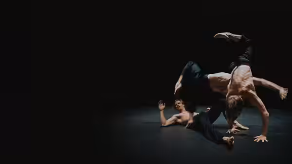 Four male dancers tangle in an acrobatic pose on a dark stage