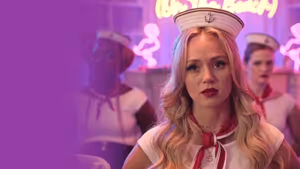 Kendell (Brec Bassinger) in a sailor costume stands before neon lights with other costumed women