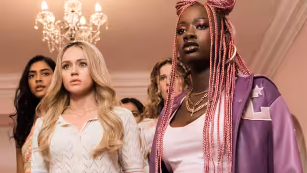 Kendell (Brec Bassinger) and a pink-braided woman stand with other women beneath a chandelier