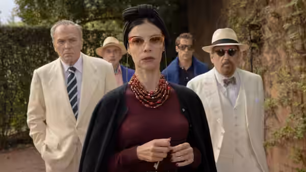A woman in sunglasses walks outdoors with several formally dressed companions