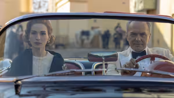 Woman and man seated in the front of a vintage convertible car on a street