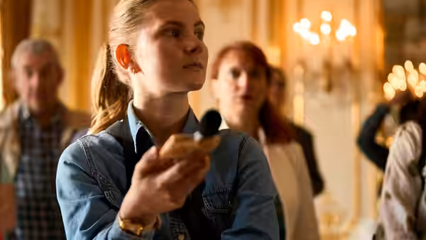 A young woman holds a small canapé in an ornate, candlelit room