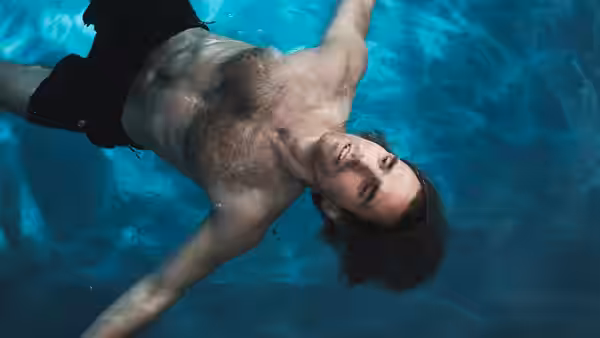 A shirtless man floats on his back in a swimming pool