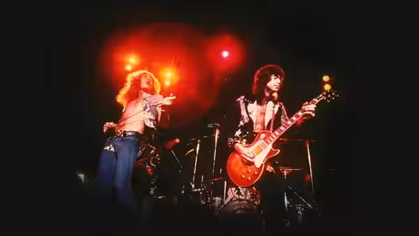 Robert Plant gesturing while Jimmy Page plays red guitar on stage