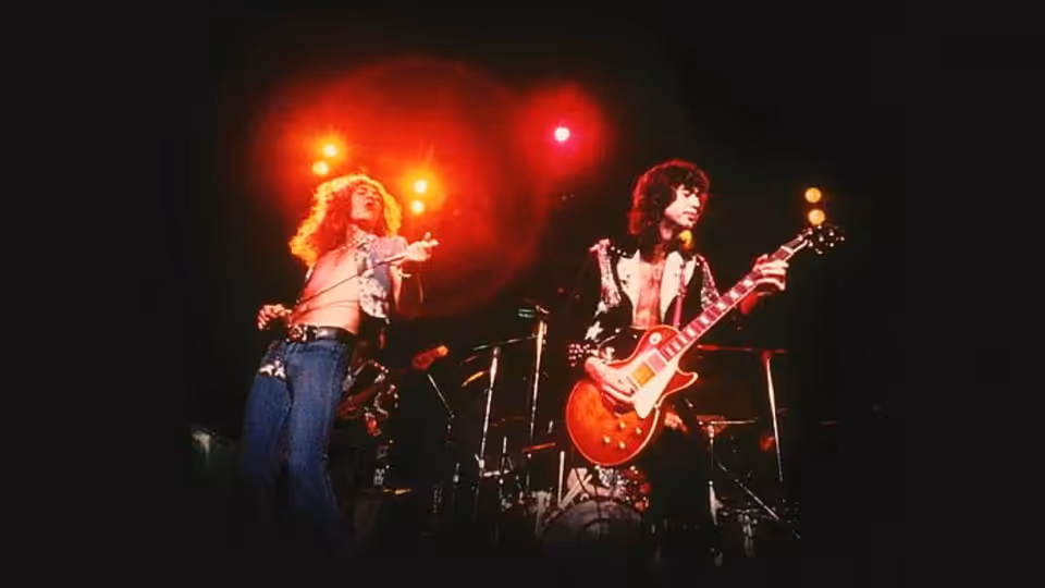 Robert Plant gesturing while Jimmy Page plays red guitar on stage