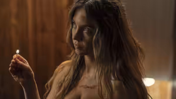 A woman with long hair holds a lit match in a wooden room