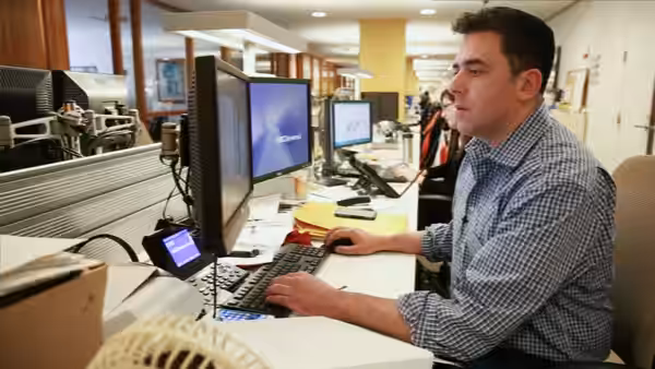 A man types at a computer workstation in a busy office