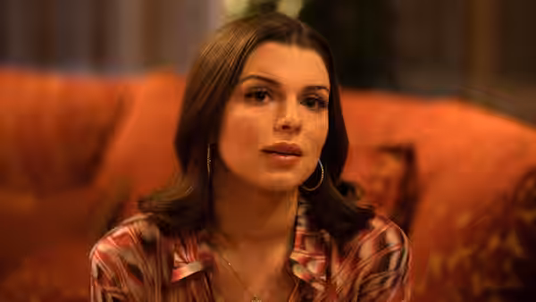Julia (Julia Fox) seated on an orange couch looking to her left