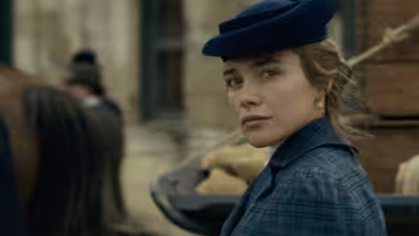 A woman in a blue hat and plaid jacket looking over her shoulder outdoors