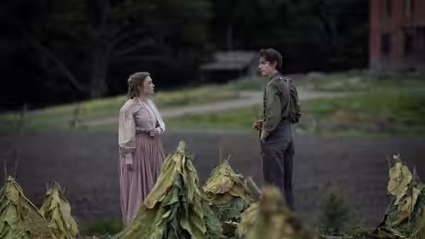 A woman in a long dress facing a young man in a harvested field
