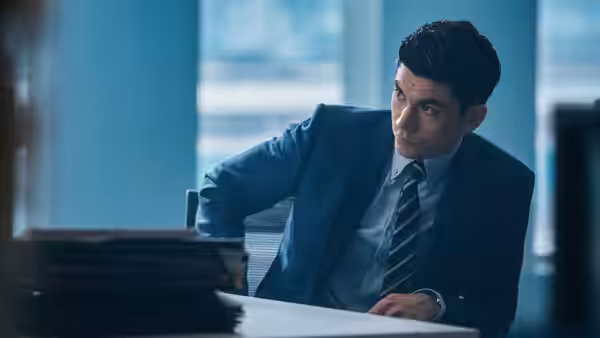 A man in a blue suit sits at a desk in an office