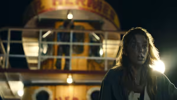 A woman stands by a boat railing at night, staring ahead in alarm
