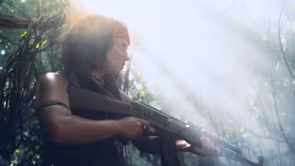 A woman with a red headband aims a rifle in misty jungle