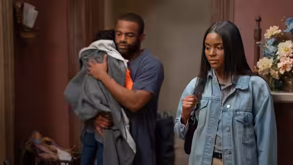 A man carries folded clothes beside a woman in a denim jacket inside a home