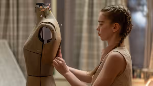 Carrie White (Summer H. Howell) adjusts a dress form in a room with curtained windows