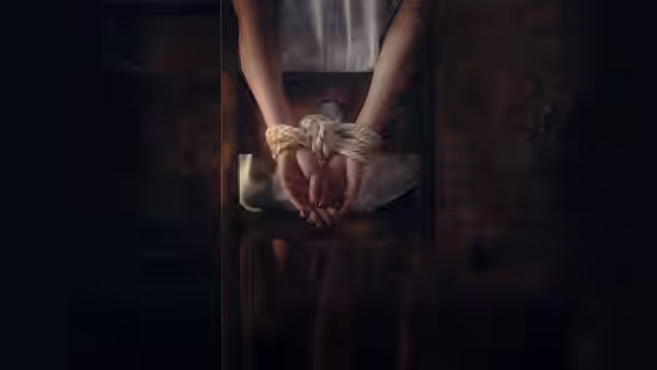 Bound hands resting on the lap of a seated person in darkness