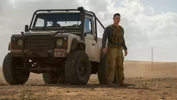 Sean (John Cena) stands beside an off-road vehicle in the desert