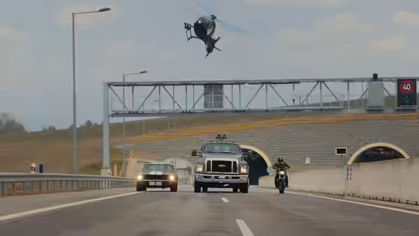 A helicopter flies over cars and a motorcyclist approaching a highway tunnel