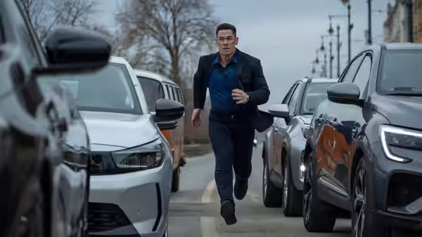 Sean (John Cena) runs between parked cars along a city street