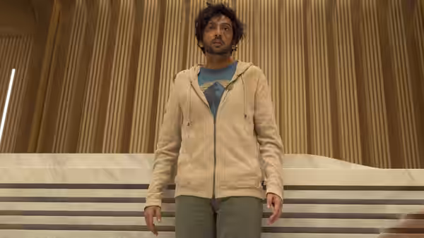Nik Dodani as Vikram Malhotra standing in a marble hall with wooden panels