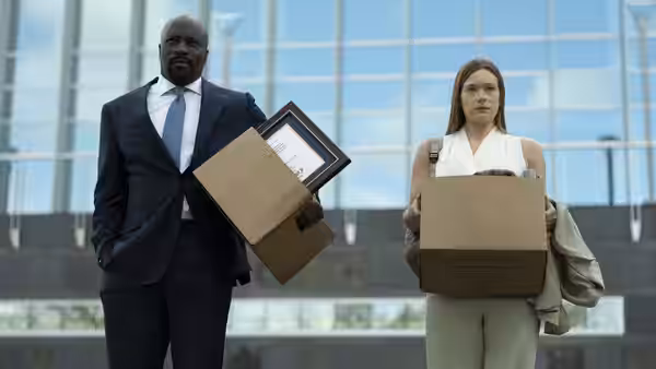 Mike Colter as Michael Price and a woman carrying boxes outside a glass building