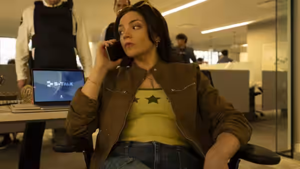 a woman on the phone seated in an open plan office with a laptop nearby