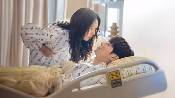 A woman in patterned pajamas leans over a man lying in a hospital bed
