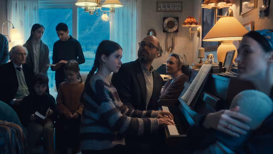 A woman playing piano as family gathers around in a living room