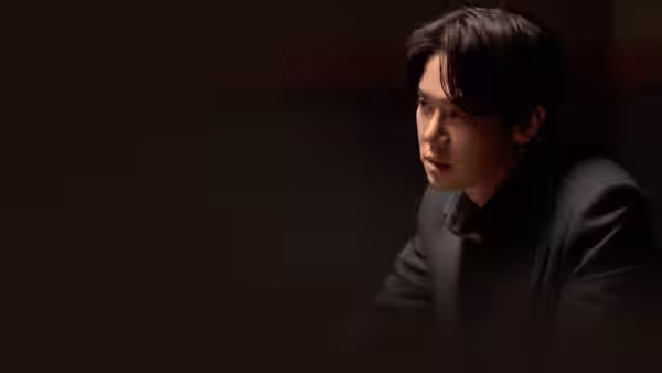 A man in a dark suit leans forward, looking offscreen